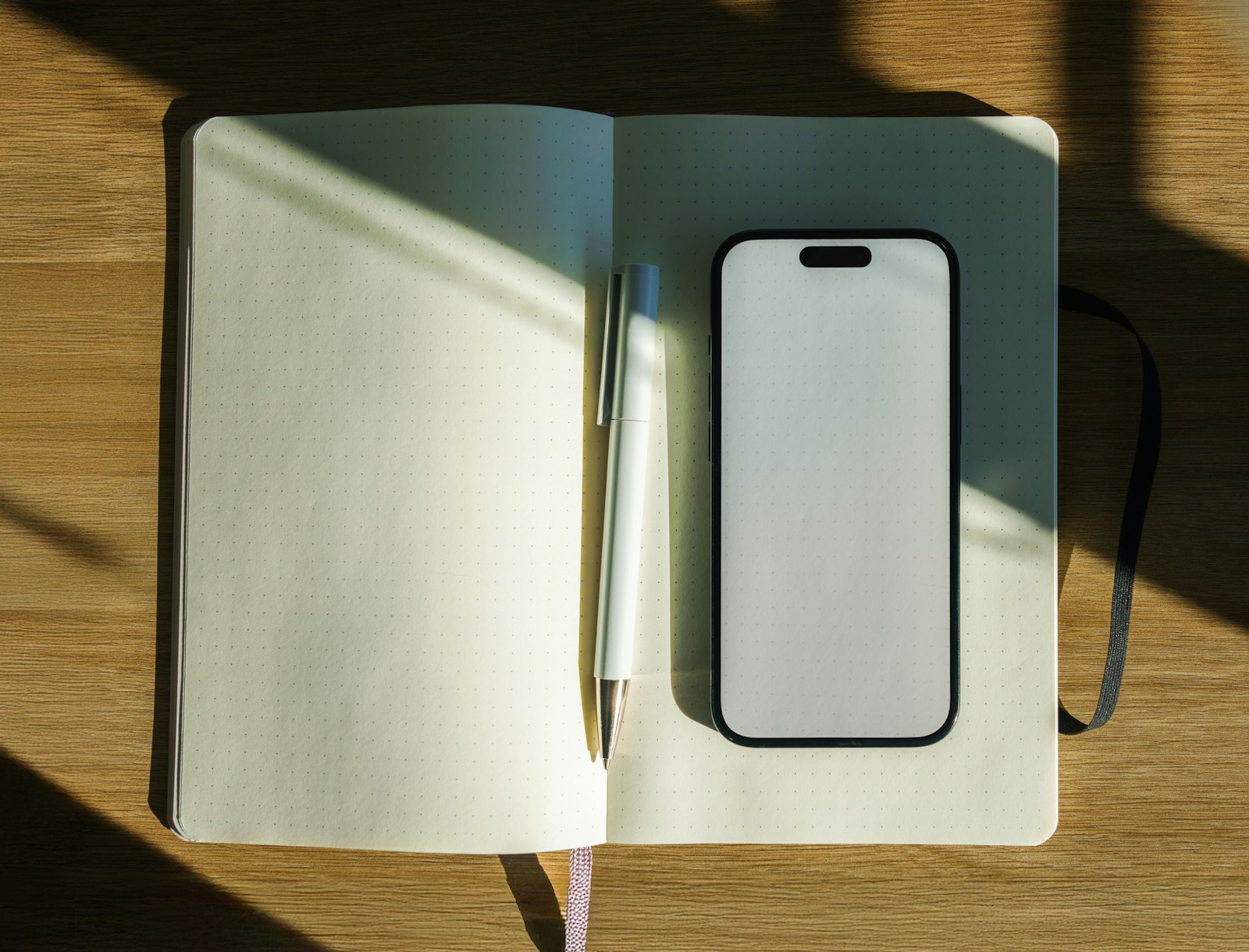 A notebook, pen, and smartphone on a sunlit desk